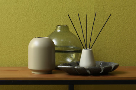 Beautiful vases and reed air freshener on wooden table near olive wall indoors, closeup