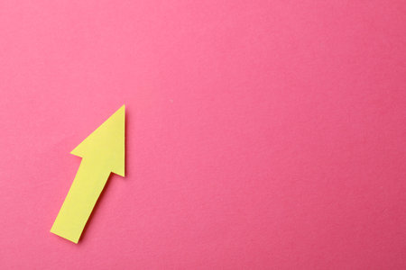 Yellow paper arrow on pink background, top view. Space for text
