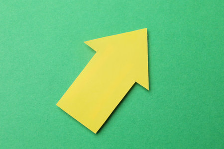 Yellow paper arrow on green background, top view