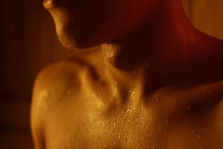 Man with drops of sweat in dark sauna, closeup