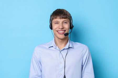 Portrait of smiling hotline operator in headset on light blue background