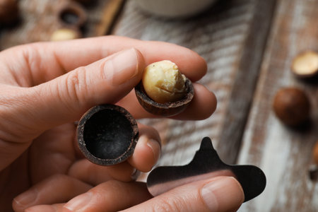 Woman holding peeled macadamia nut and metal key at wooden table, closeup
