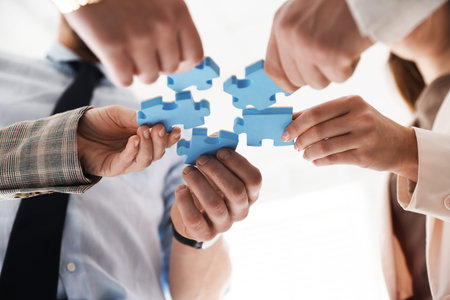 Team building. Group of businesspeople putting puzzle pieces together indoors, low angle view
