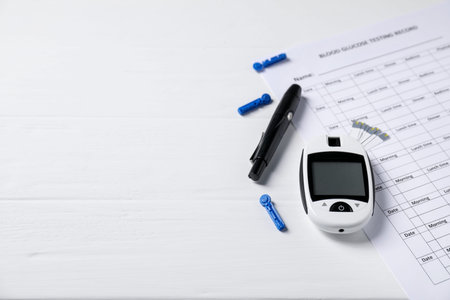 Diabetes. Digital glucometer, pen, test strips, lancets and record form on white wooden table,...