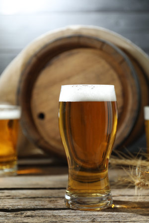 Glasses with fresh beer, spikes and barrel on wooden table, closeup
