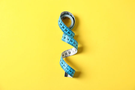 One measuring tape on yellow background, top view
