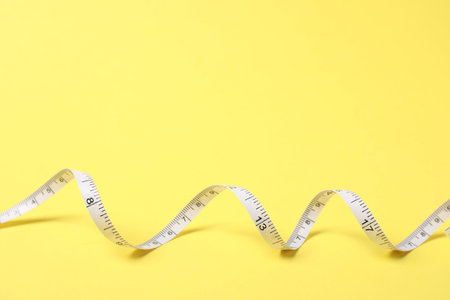 One measuring tape on yellow background, closeup. Space for text
