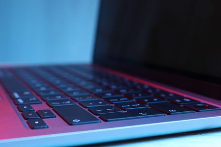 Stylish modern laptop in neon lights on white background, closeup