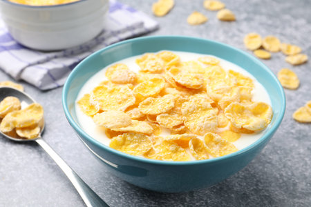 Tasty corn flakes with milk in bowl served on grey table, closeup