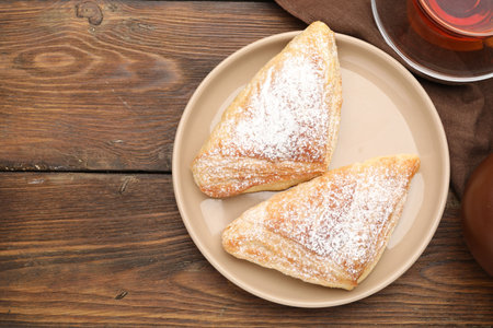 Tasty puff pastries with powdered sugar and tea on wooden table, flat lay. Space for text