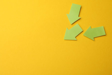 Green paper arrows on yellow background, flat lay. Space for text