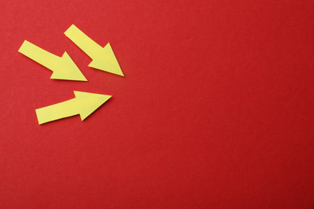 Yellow paper arrows on red background, flat lay. Space for text