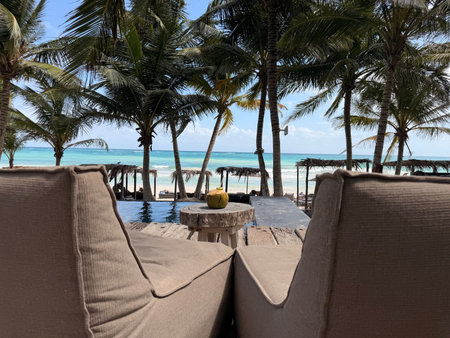 Refreshing coconut drink on table and armchairs near swimming pool at tropical resort