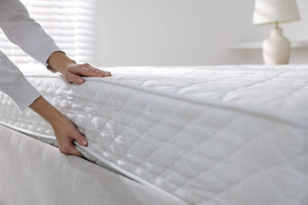 Woman touching soft mattress on bed indoors, closeup