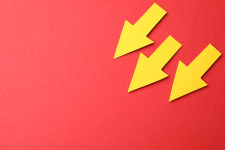 Yellow paper arrows on red background, flat lay. Space for text