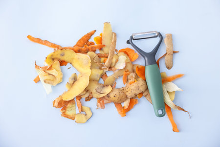 Pile of organic waste and peeler on grey table, flat lay