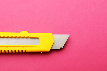 One sharp paper knife on pink background, closeup. Space for text