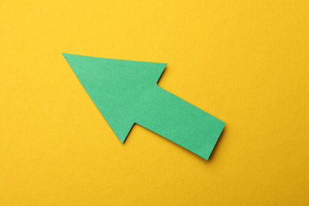 Green paper arrow on yellow background, top view