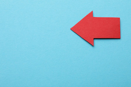 Red paper arrow on light blue background, top view. Space for text