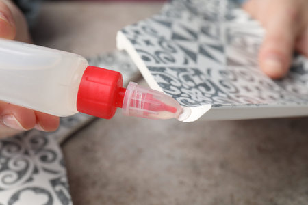 Woman gluing together pieces of broken plate at grey table, closeup