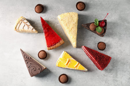 Pieces of different tasty cakes and candies on grey table, flat lay