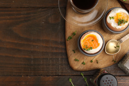 Tasty breakfast with soft boiled eggs, microgreens, spices and coffee on wooden table, flat lay. Space for text