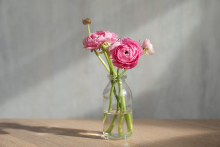 Beautiful flowers in vase on wooden table against light background. Space for text