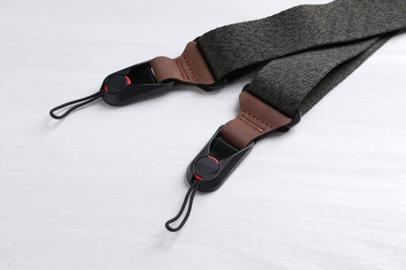 Modern black camera strap on white wooden table, closeup