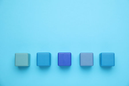 Empty wooden cubes on light blue background, flat lay. Space for text