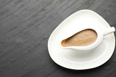 Tasty turkey gravy in sauce boat on dark textured table, top view. Space for text