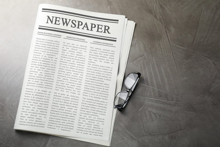 Newspaper and glasses on grey table, flat lay