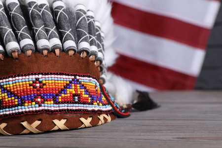Native American chief headdress (feathered war bonnet) on wooden surface, closeup. Space for text