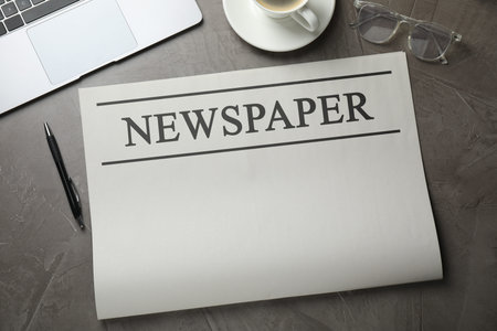Newspaper, laptop, pen, glasses and coffee on grey textured table, flat lay