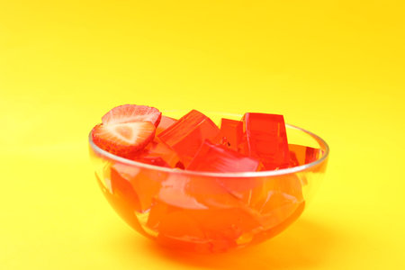 Tasty jelly cubes with strawberry slices on yellow background, closeup. Space for text