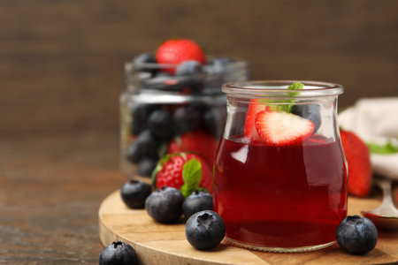 Yummy jelly in glass jar, blueberries, strawberries and mint on wooden table, closeup. Space for text