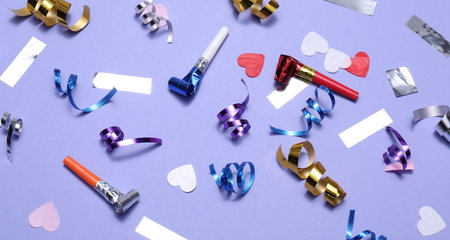 Shiny party streamers, horns and confetti on violet background, flat lay