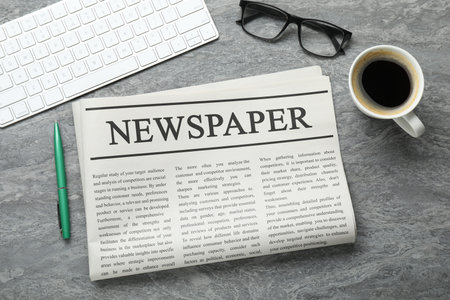 Newspaper, computer keyboard, pen, glasses and coffee on grey table, flat lay