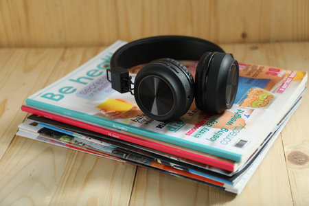Many lifestyle magazines and headphones on wooden table, closeup