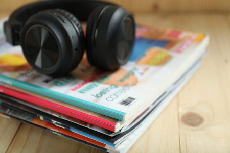 Many lifestyle magazines and headphones on wooden table, closeup