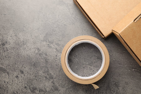 Roll of masking tape and boxes on grey table, flat lay. Space for text
