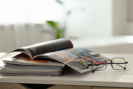 Many lifestyle magazines and glasses on white table indoors, closeup. Space for text