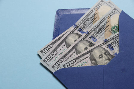 Envelope with dollar banknotes on light blue background, closeup. Space for text