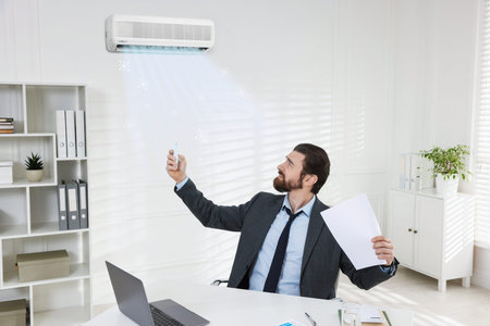 Man suffering from heat turning on air conditioner in office. Comfortable workplace environment