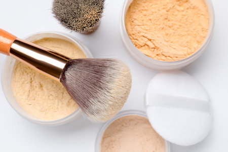 Loose face powders, puff and makeup brushes on white background, flat lay