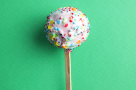 Tasty cake pop with sprinkles on green background, top view