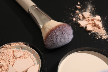Makeup brush and face powder on black background, closeup