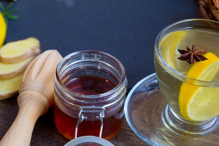 Glass cup of hot tea with mint, honey, ginger and lemon on dark background.