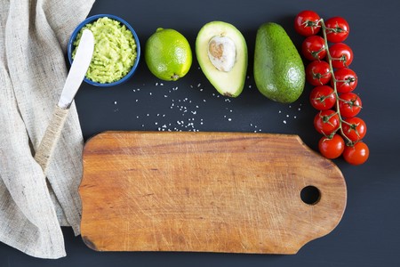 Traditional latinamerican mexican sauce guacamole in ceramic bowl and ingredients on dark background. Old cutting board. Top view. Flat lay. Copy space.の写真素材