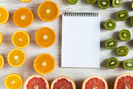 Flat lay Top view notebook with sliced kiwi, orange, grapefruit and mandarin on light background....