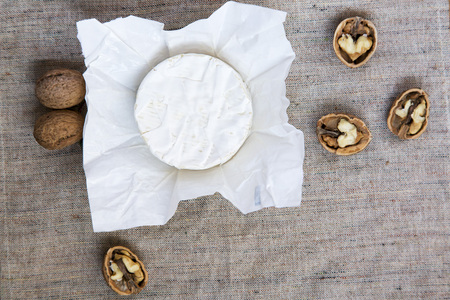 Round cheese camembert or brie in paper with walnuts. Copy text. Flat lay. Top view. From above. Obsolete burlap texture.の写真素材